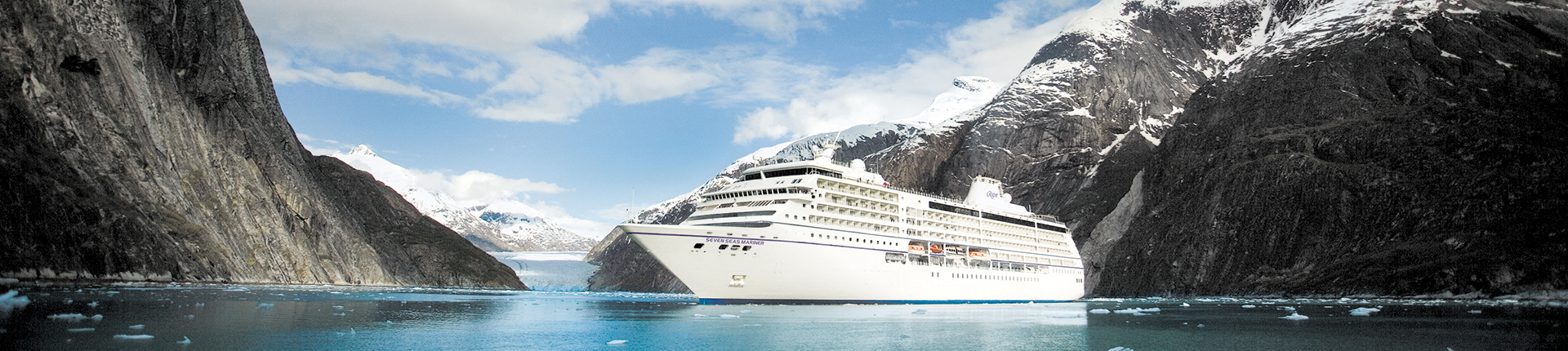Regent Mariner at sea in Alaska with snow capped mountains in the background and ice floating in the ocean.